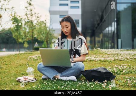 Verwendet Laptop. Eine junge Asiatin ist tagsüber draußen Stockfoto
