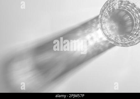 Ein Glas mit Wasser und scharfen Schatten, kaustischer Effekt, wenn Licht auf hellem Hintergrund durchdringt Stockfoto