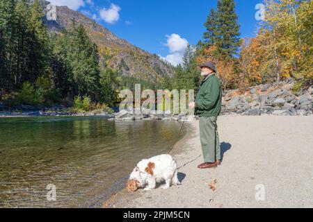 Leavenworth, Washington, USA. Blick auf eine Fußgängerbrücke über den Wenatchee River. Ein Mann, der mit seinem Kavalier König Charles Spaniel spaziert. Stockfoto