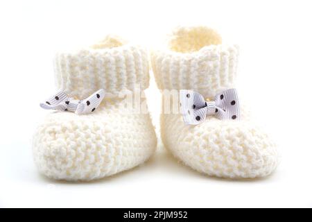 Gestrickte weiße Babyschühchen mit Schleifen mit Punktmuster auf einem grau isolierten Hintergrund. Hintergrund. Für Text. Foto in hoher Qualität Stockfoto