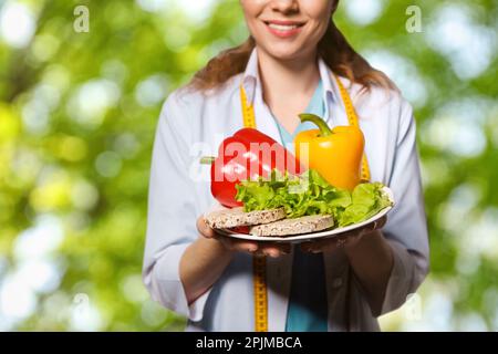 Ernährungswissenschaftler mit gesunden Produkten auf verschwommenem grünen Hintergrund, Nahaufnahme Stockfoto