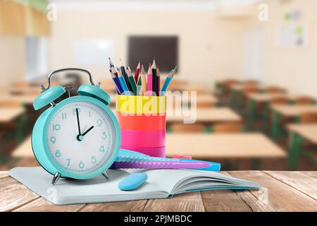 Türkisfarbener Wecker und verschiedene Schreibwaren auf Holztisch im Klassenzimmer Stockfoto