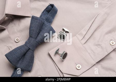 Elegante blaue Fliege und Manschettenknöpfe auf beigefarbenem Hemd, Draufsicht Stockfoto