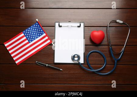 Stethoskop, rotes Herz, Klemmbrett und amerikanische Flagge auf Holztisch, flach liegend Stockfoto