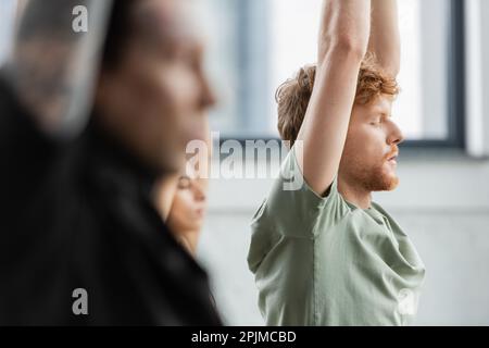 Seitenansicht eines rothaarigen Mannes, der Yoga in der Nähe von multiethnischen Personen in der Yoga-Gruppe praktiziert, Stockbild Stockfoto