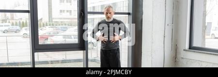 Reifer Mann in Sportbekleidung, der den Bauch berührt, während er Yoga im Unterricht übt, Banner, Stock Image Stockfoto