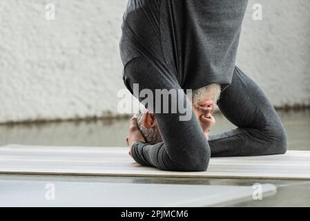 Reifer Mann, der unterstütztes Kopfständer-Asana auf der Matte im Yoga-Studio macht, Stock Image Stockfoto