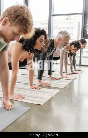 Multiethnische Menschen stehen in Plank Asana auf Matten im Yoga-Kurs, Stockbild Stockfoto
