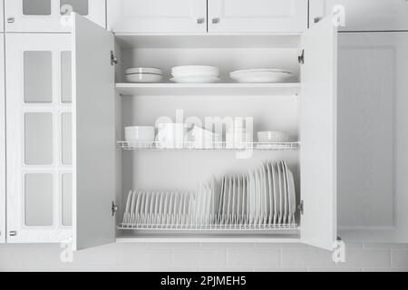 Offener Schrank mit verschiedenen sauberen Tellern und Schüsseln in der Küche Stockfoto