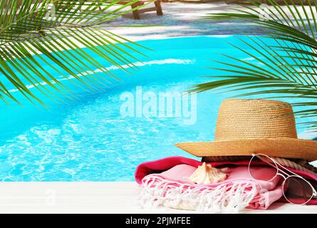 Strandtuch, Hut und Sonnenbrille auf weißer Holzfläche in der Nähe des Außenpools. Platz für Text Stockfoto