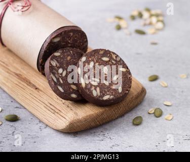 Schokoladenwurst mit Haferbrei und Samen auf grauem, strukturiertem Hintergrund. Köstliches, gesundes veganes Dessert Stockfoto