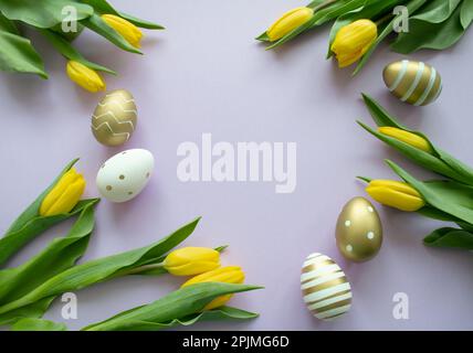 Ostereier aus Gold, weiße Farbe mit Muster und gelbe Tulpen auf pinkfarbenem Hintergrund. Speicherplatz kopieren. Stockfoto