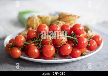 Frische Bio-rote reife Kirschtomaten mit reifer Karambola, auch bekannt als Sternfrucht auf einem weißen Teller auf dem Tisch, Nahaufnahme Stockfoto