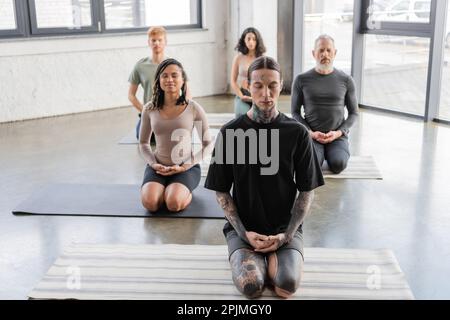 Gemischtrassige Gruppe von Menschen, die mit geschlossenen Augen in Thunderbolt Yoga-Pose meditieren, Stockbild Stockfoto