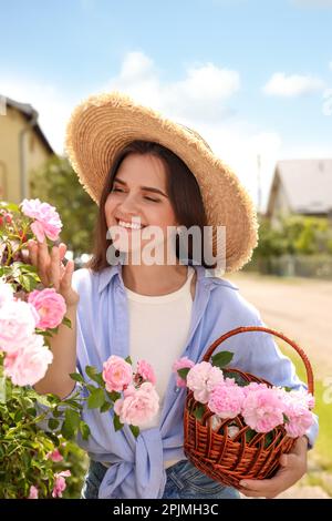 Glückliche junge Frau mit einem Korb mit pinkfarbenen Teerosen im blühenden Garten Stockfoto