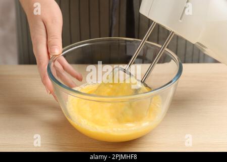 Eine Frau, die Eier mit einem Mixer am Holztisch schlägt, Nahaufnahme Stockfoto