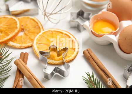 Keksschneider, getrocknete Orangenscheiben, Zimtstangen und Eier auf einem weißen Tisch. Weihnachtskekse Stockfoto