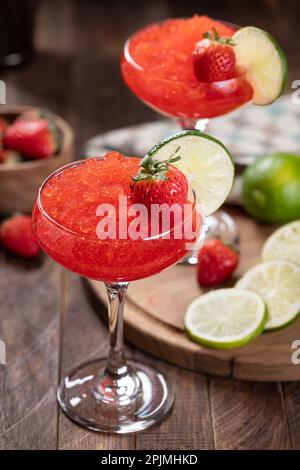 Gefrorener Erdbeerdaiquiri garniert mit Erdbeeren und Limettenscheiben auf rustikalem Holzhintergrund Stockfoto