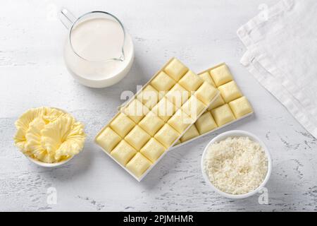 Zutaten für die Zubereitung selbstgemachter Süßigkeiten: Weiße Schokolade, Butter, schwere Sahne und Kokosflocken auf hellgrauem Hintergrund, Draufsicht Stockfoto