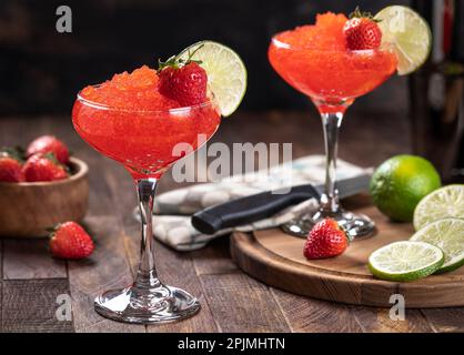 Gefrorener Erdbeerdaiquiri garniert mit Erdbeeren und Limettenscheiben auf rustikalem Holzhintergrund Stockfoto