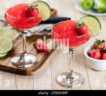 Gefrorener Erdbeerdaiquiri, garniert mit Erdbeeren und Limettenscheiben auf einem Holztisch Stockfoto