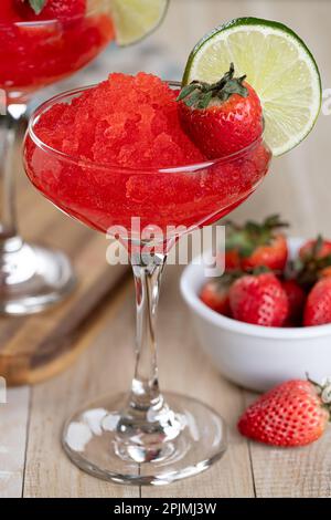 Nahaufnahme von gefrorenem Erdbeerdaiquiri garniert mit Erdbeeren und Limettenscheiben auf einem Holztisch Stockfoto