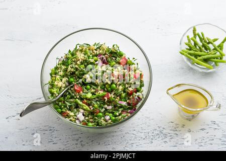 Traditioneller Salat aus dem Nahen Osten oder arabischem Tabbouleh mit Bulgur, Tomaten, Spargel, grünen Erbsen und Grünen auf hellgrauem Hintergrund, Draufsicht. Heilung Stockfoto