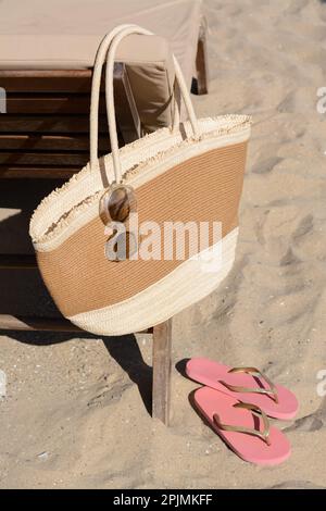 Strohbeutel mit Sonnenbrille und Flip Flops auf Sand. Strandaccessoires Stockfoto