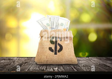 Leinenbeutel mit Dollarzeichen und Banknoten auf Holztisch im Innenbereich Stockfoto