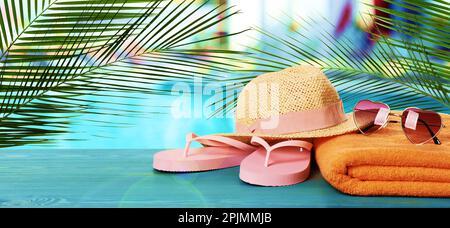 Strandtuch, Flip-Flops, Strohhut und herzförmige Sonnenbrille auf hellblauer Holzfläche in der Nähe des Außenpools. Bannerdesign Stockfoto