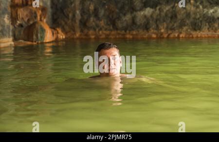 Ein Mann badet in einer Höhle im Freien, schmutzige heiße Quellen. Thermalbad. Gesunder natürlicher Lehm. Gelber grüner Schlamm. Wellness-Behandlungen, Entspannung. Fa Stockfoto