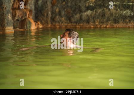 Ein Mann badet in einer Höhle im Freien, schmutzige heiße Quellen. Thermalbad. Gesunder natürlicher Lehm. Gelber grüner Schlamm. Wellness-Behandlungen, Entspannung. Fa Stockfoto