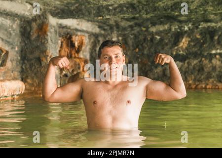 Kräftige Muskeln baden in einer Höhle im Freien, schmutzige heiße Quellen. Thermalbad. Gesunder natürlicher Lehm. Gelber grüner Schlamm. Wellness-Programm Stockfoto