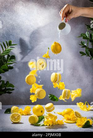 Zitronen-Makronen und gelbe Freesien fliegen auf hellem Hintergrund. Köstliches französisches Dessert Stockfoto