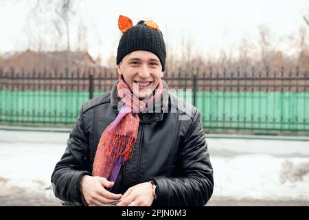 Ein fröhlicher junger Mann mit Tigerohren auf dem Kopf lacht, während er in die Kamera schaut. Zur Feier von Maslenitsa. 22. Februar 2015, Kolomna, Moskau reg Stockfoto