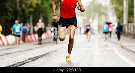 Männlicher Läufer läuft Marathonrennen, joggt nach Regen auf nassem Asphalt, Sommersportspiele Stockfoto