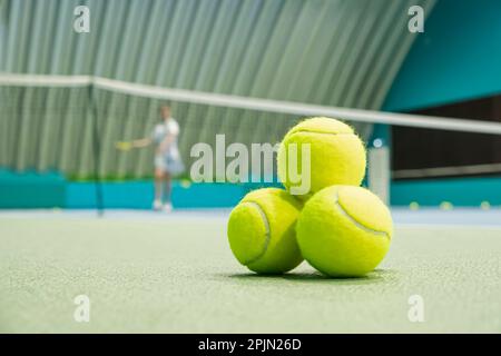 Konzept eines sportlichen Lebensstils. Tennisbälle auf dem Boden vor dem Hintergrund eines Mädchens, das Tennis in der Tennishalle spielt Stockfoto