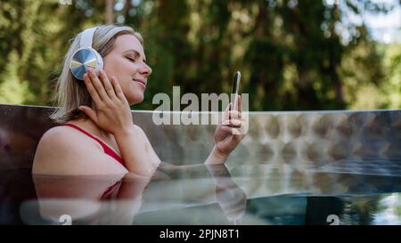 Reaxed Woman mit Kopfhörern, die in der Badewanne im Freien Musik hören. Stockfoto