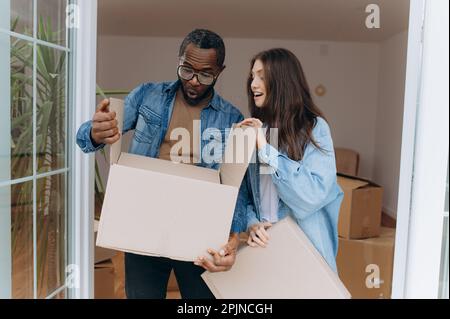 Das glückliche Paar öffnet eine Pappschachtel mit Sachen. Auspacken des Kartons während des Transports Stockfoto