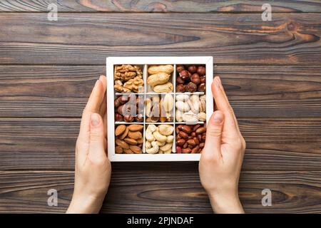 Junge Frau, die eine Kiste mit anderen Nüssen hält, Nahaufnahme. Nahaufnahme, Kopierbereich, Draufsicht, flach liegend. Walnuss, Pistazien, Mandeln, Haselnüsse und Cashews. Stockfoto