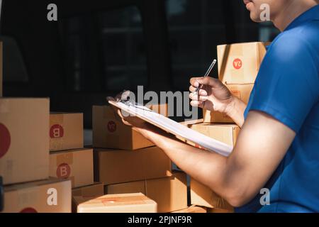 Der Zusteller unterzeichnet die Checkliste auf dem Klemmbrett. Männlicher Kurier, der auf das Klemmbrett schreibt und den Barcode scannt. Der reife Mann aktualisiert die Checkliste der Entbindung im Lieferwagen Stockfoto