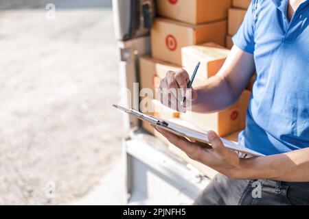 Der Zusteller unterzeichnet die Checkliste auf dem Klemmbrett. Männlicher Kurier, der auf das Klemmbrett schreibt und den Barcode scannt. Der reife Mann aktualisiert die Checkliste der Entbindung im Lieferwagen Stockfoto