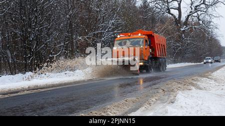 Ein großes Auto mit einem Pflug befreit die Straße von Schnee. Die Sonderausrüstung Orange Cargo kämpft im Winter mit den Elementen. Beseitigung der Auswirkungen von t Stockfoto