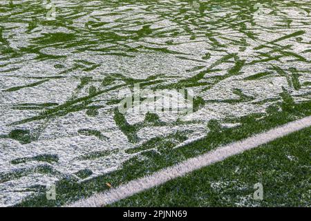 Das Fußballfeld mit Kunstrasen ist mit einer leichten Schneeschicht bedeckt. Frühling. Grünes Gras auf dem Fußballfeld ist von zu sehen Stockfoto