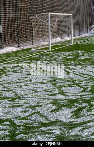 Fußballfeld im Winter, künstliches Gras auf freiem Schnee im Ferntor und Netz. Stockfoto
