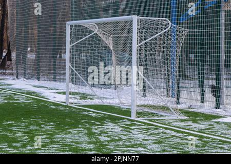 Fußballfeld im Winter, künstliches Gras auf freiem Schnee im Ferntor und Netz. Stockfoto