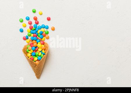 Waffelkonus voller traditioneller Süßigkeiten, die auf farbigen Hintergrund fallen, mit Platz für Kopien. Frohes Weihnachtsangebot. Stockfoto