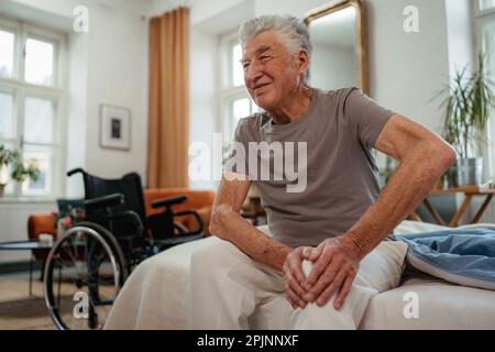 Porträt eines Seniorenmannes mit Knieschmerz, der auf einem Bett sitzt. Stockfoto