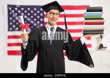 Älterer Mann mit einem Diplom und einem Stapel Bücher, der vor einer US-Flagge vor der Kamera lächelt Stockfoto