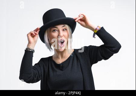 Lächelnde blonde Frau mit schwarzem Hut isoliert auf weißem Hintergrund. Junge Frau mit wunderschönem Lächeln, glücklich und aufgeregt. Stockfoto